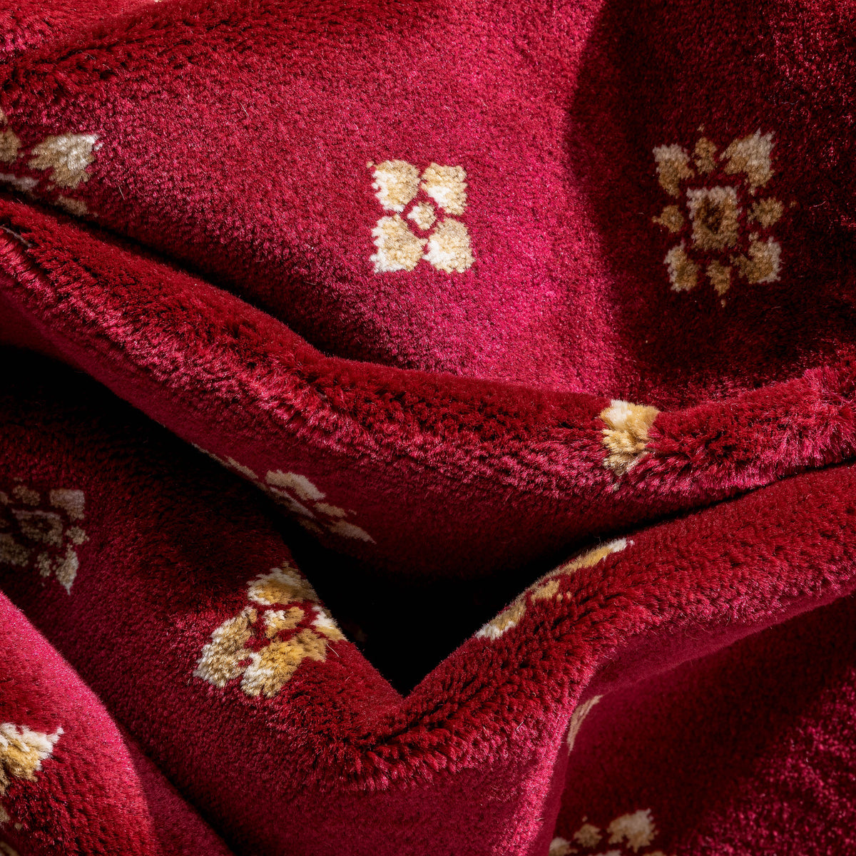 A close-up of a plush, deep red fleece blanket with small beige and cream floral patterns woven into the fabric.