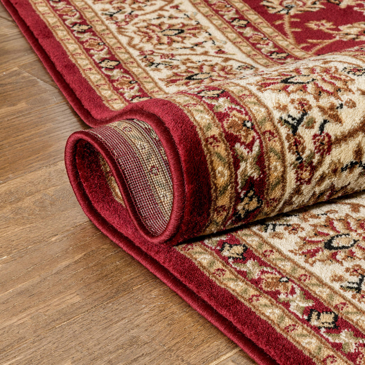 Rolling up a patterned red and beige rug on a wooden floor
