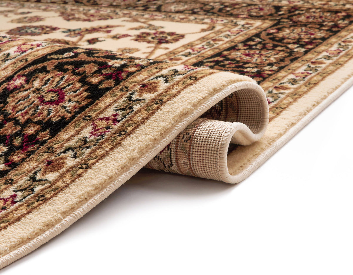A close-up of a rolled area rug showing its detailed traditional pattern in beige, brown, black, and muted red tones, with the underside texture visible.