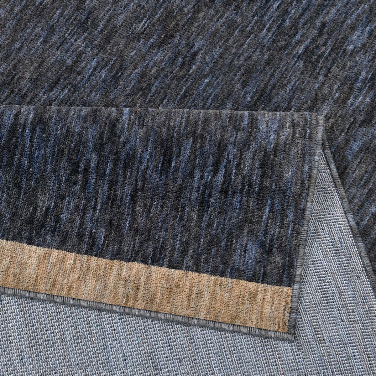 COD-13 Well Woven Moor Midnight Charcoal Area Rug - Close-up of the heathered blue and gray pile rug with a camel brown striped edge.