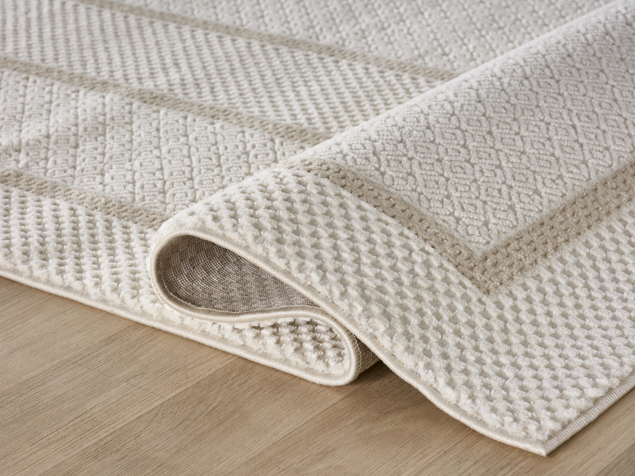 Lafayette Frame ivory and cream border area rug, rolled to show pile depth and the jute backing