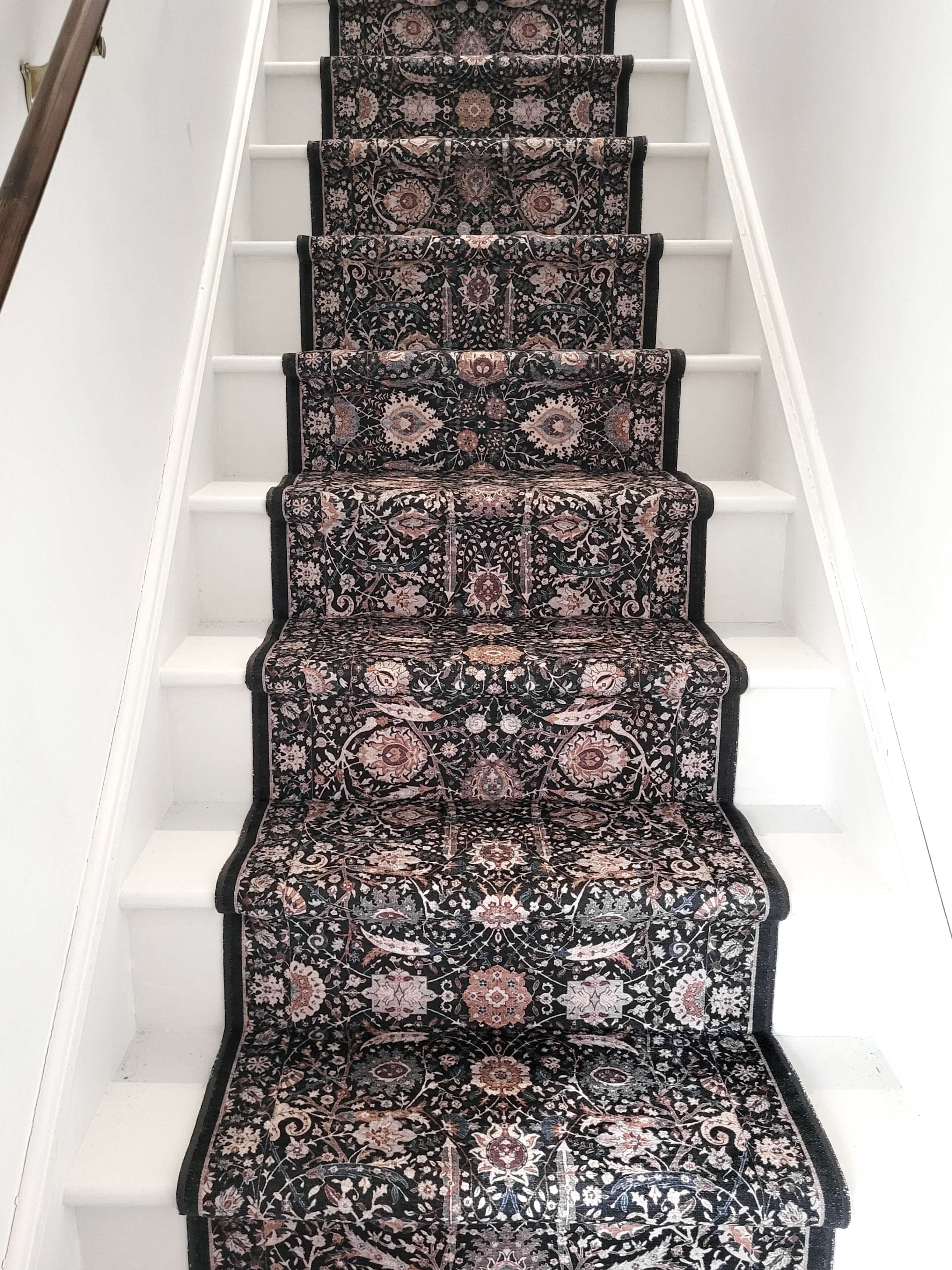 Staircase with a patterned charcoal grey/ black floral carpet runner.