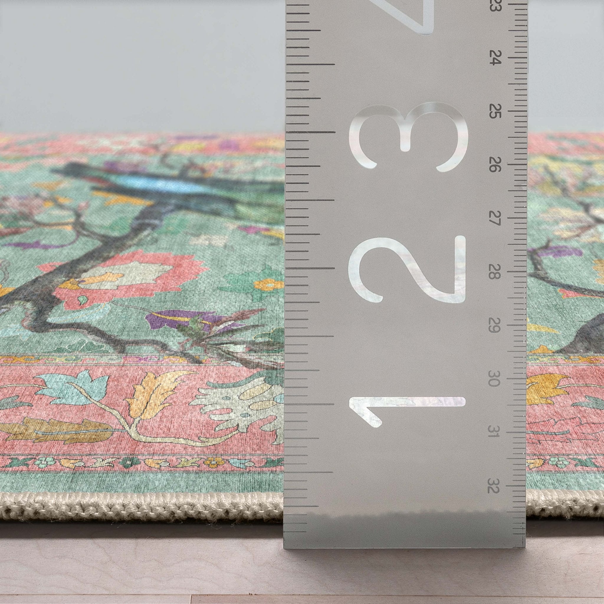 Close-up of the green rug's edge and thickness next to a ruler showing low-pile washable construction.