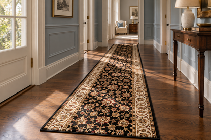 A long runner rug with an ornate floral pattern in black, beige, and cream, displayed on a hardwood floor in a bright hallway with blue-gray walls.
