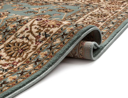 A close-up of a rolled area rug showing its detailed traditional pattern in beige, brown, and muted teal, with a matching border on a white background.