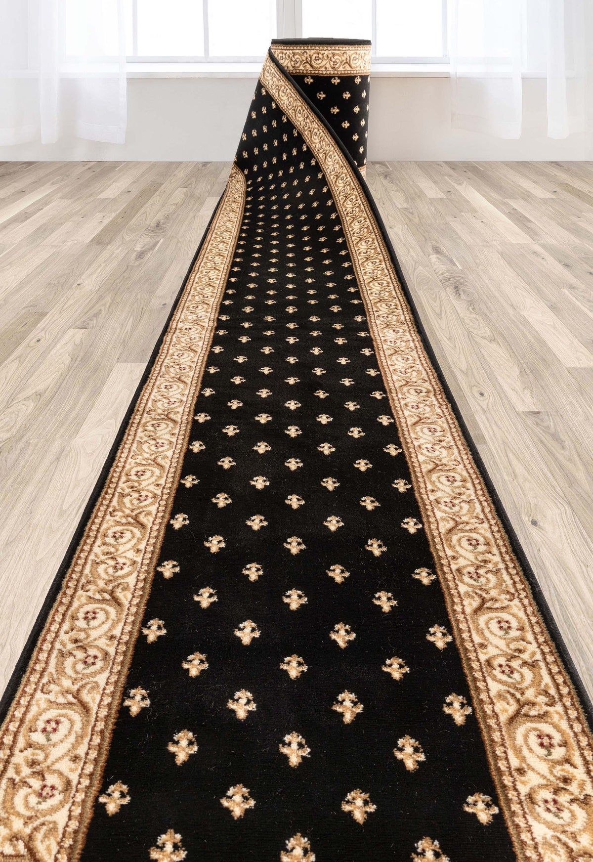 A long black runner rug with ornate gold and beige borders and small gold motifs, shown laid out on a light wood floor in a bright room.