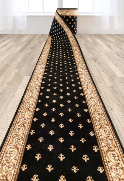 A long black runner rug with ornate gold and beige borders and small gold motifs, shown laid out on a light wood floor in a bright room.