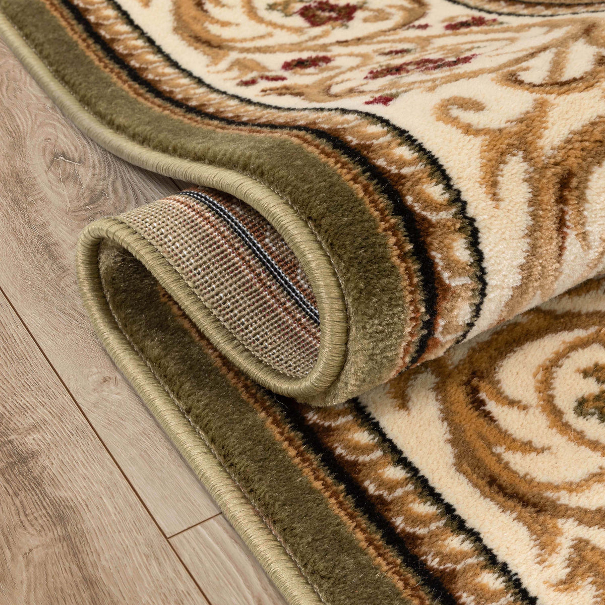 A close-up of a rolled area rug with a traditional ornamental pattern in beige, brown, olive green, and black, shown on a light wood floor.