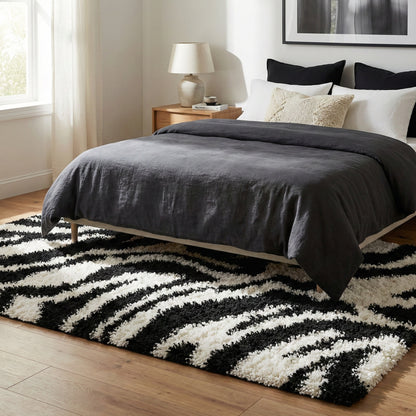 7033 - Bedroom with a zebra pattern shag rug, bed with dark gray comforter, and nightstand with lamp.