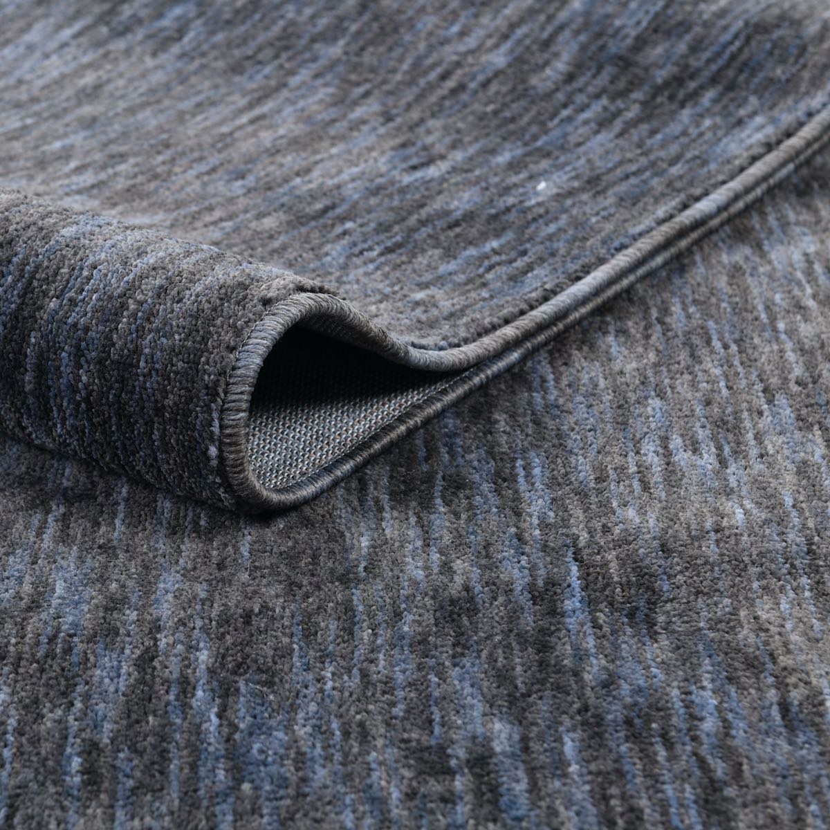 COD-13 Well Woven Moor Washable Rug: Close-up of a textured charcoal black and slate blue eco-friendly rug with a rolled edge.