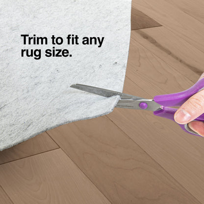 PAD-1 - Well Woven Premium Felt Non-Slip Rug Pad - Person using scissors to trim a felt rug pad on a wooden floor with text 'Trim to fit any rug size".