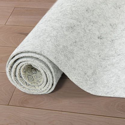 PAD-1 - Well Woven Premium Felt Non-Slip Rug Pad - Rolled-up gray rug pad 1/4" thick on a wooden floor. The top of the pad is felt and the bottom is non-slip rubber