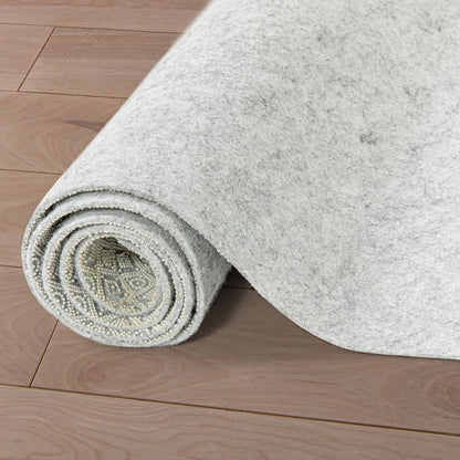 PAD-1 - Well Woven Premium Felt Non-Slip runner rug pad - Rolled-up gray runner rug pad 1/4" thick on a wooden floor. The top of the pad is felt and the bottom is non-slip rubber